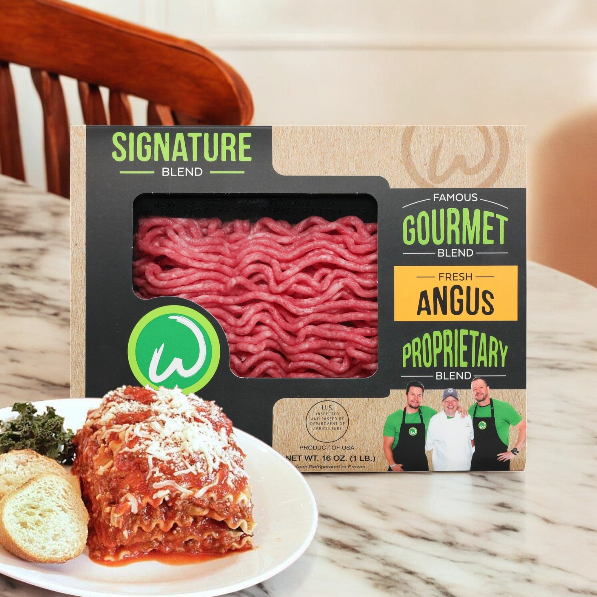 Wahlburgers Signature Blend Loaf, 16 oz, is placed next to a plate with lasagna, a bread roll, and salad on a table.