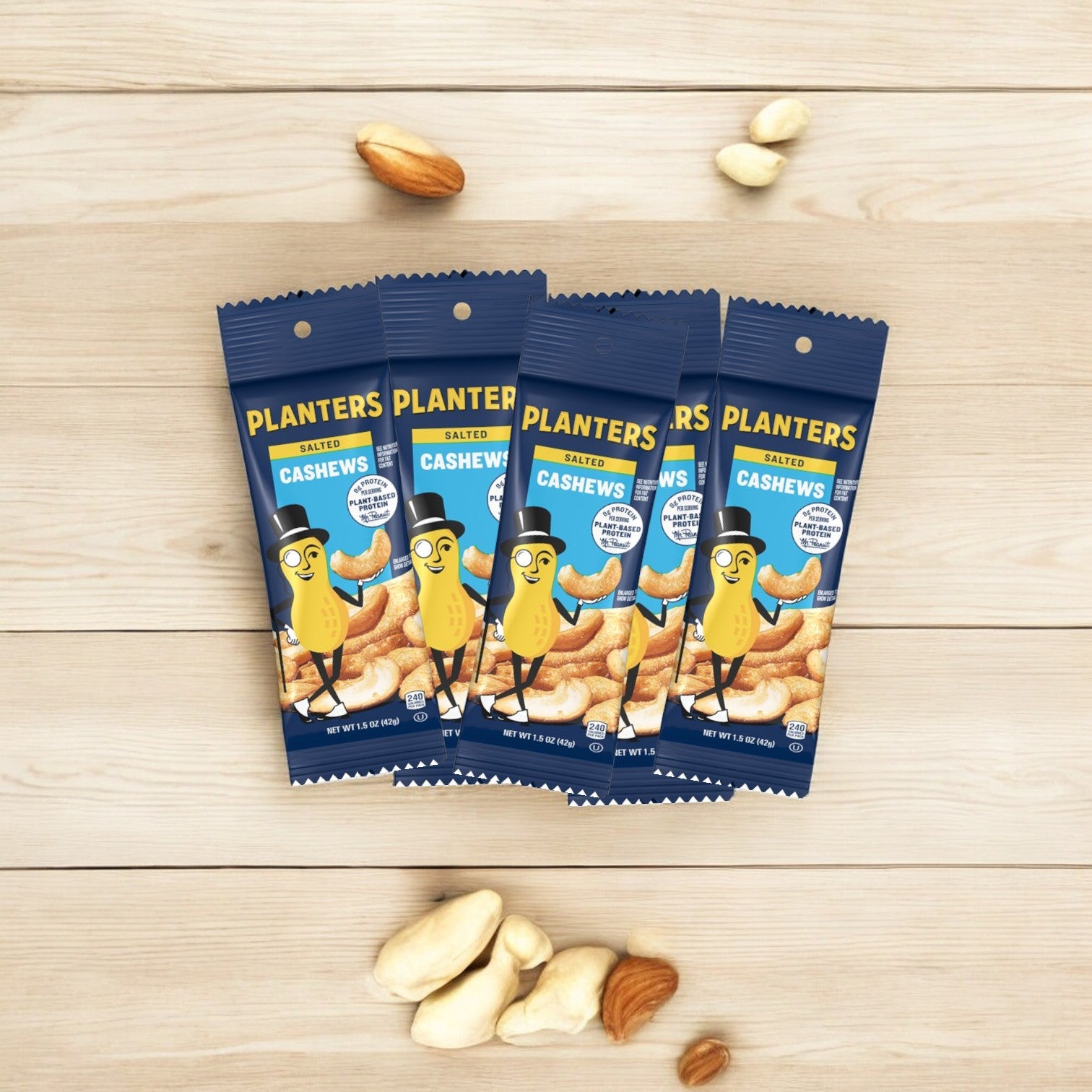 Five packs of Planters Cashews - 5 bags - 1.5 oz each arranged on a wooden surface, surrounded by scattered cashews and cashew pieces. Planters guarantees these quality snacks deliver the perfect crunch every time.