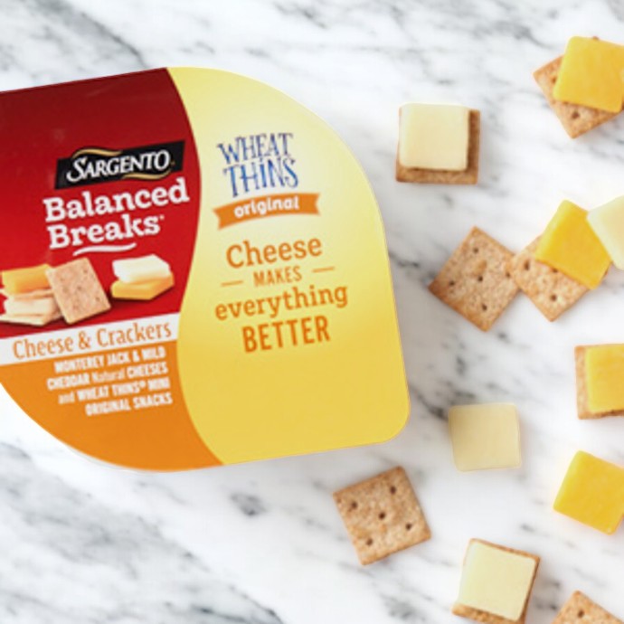 A package of Easy Lunches Sargento Balanced Breaks Cheese & Mini Wheat Thin Crackers lies on a marble surface, offering Monterey Jack and mild cheddar cheeses with mini Wheat Thin crackers. This delicious snack pack features pieces of cheese and crackers scattered around the package.