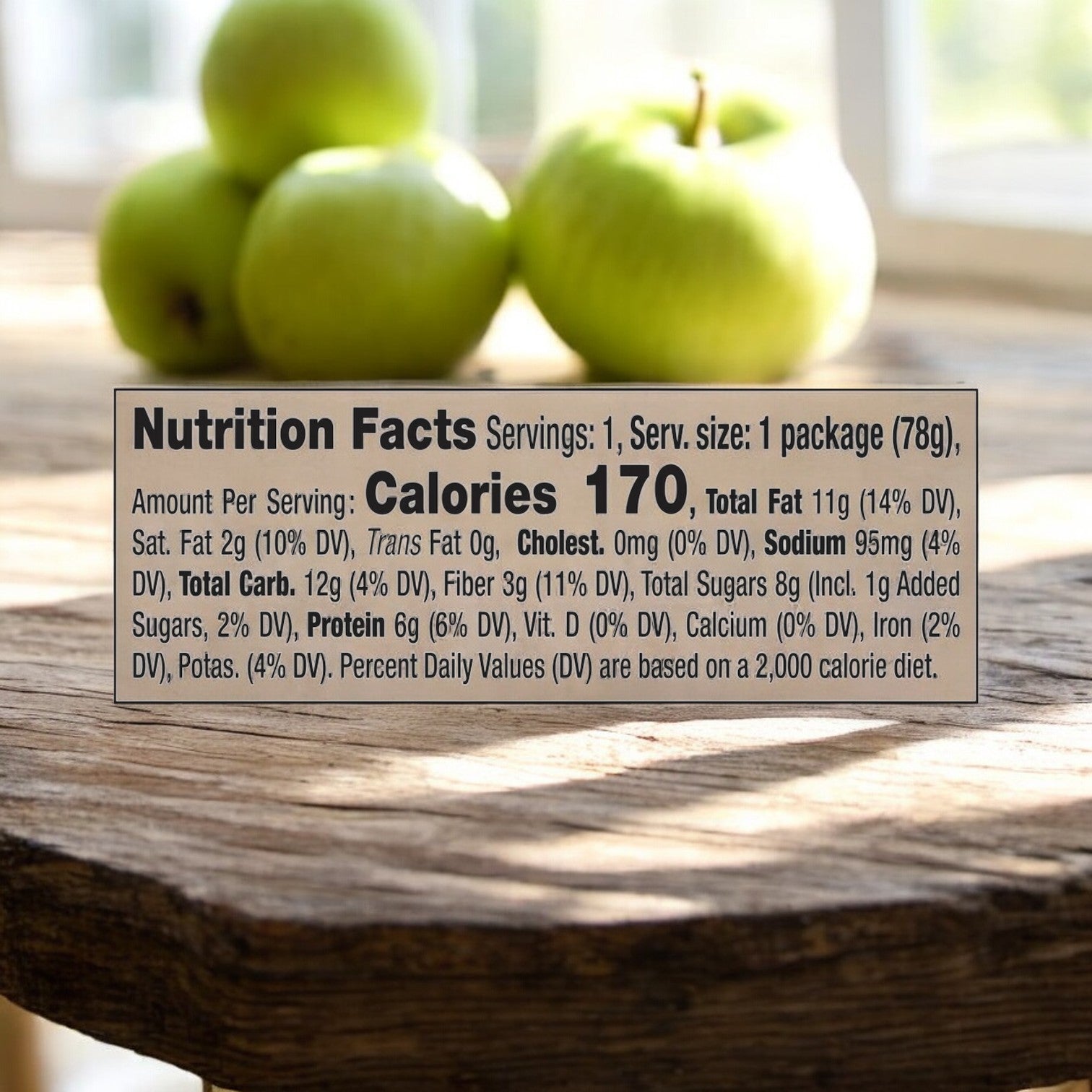 The Nutrition Facts label reveals details such as 170 calories per serving, 12g total carbs, 6g protein, along with nutrients' daily values. In the background, blurred sliced apples suggest that Dippin' Stix Sliced Apples & Peanut Butter - 2.75 oz - 1 Count by Dippin' Stix makes an ideal nutritious snack when paired with peanut butter.