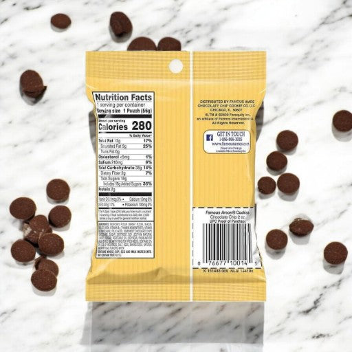 A yellow Famous Amos snack pouch with nutrition facts on the back lies on a marble surface, surrounded by small scattered Famous Amos Chocolate Chip Cookies - 2oz - 1 Count, known for their crispy edges and chewy centers.