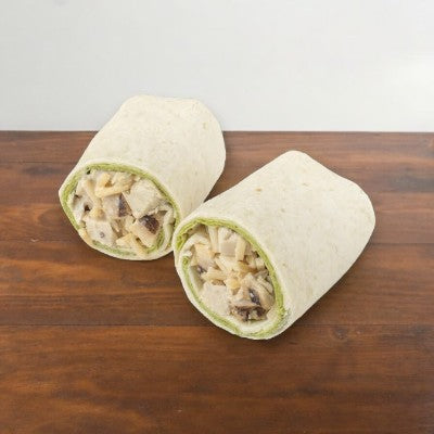 Two halves of an E.A. Sween Chicken Caesar Wrap -1 Count, filled with diced chicken, cheese, and other ingredients, sit on a wooden surface.