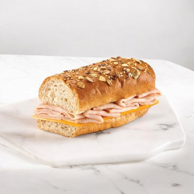 An E.A. Sween Smoked Turkey & Cheddar Sub Sandwich on a rustic oat-topped roll, placed on a marble surface.