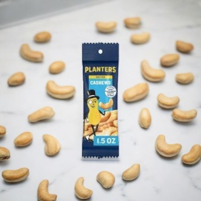 A 1.5 oz packet from Planters Cashews - 5 bags, a testament to quality snacks by Planters, is surrounded by scattered cashew nuts on a white marble surface.