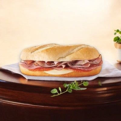 An Italian Style Sub from E.A. Sween, featuring sliced roast beef, cheese, and small greens, sits on a wooden table against a neutral background.