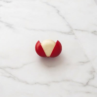 A small round piece of Mini Babybel Original Semisoft Cheese, partially wrapped in red wax, sits on a marble surface, showcasing its creamy taste.