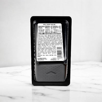 Plastic container with a label displaying nutritional facts and ingredients for a Dill Egg Salad On Homestyle White Bread Sandwich Wedge, placed on a marble surface.