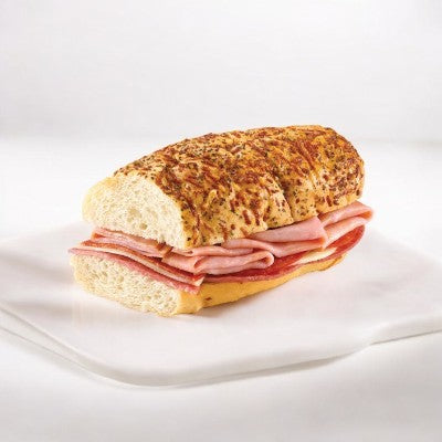 The Artisan Italian Style Sub from E.A. Sween, featuring layers of sliced ham and salami on a seasoned bread roll, served on a white plate.