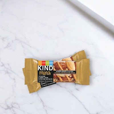 Two Kind Minis Caramel Almond & Sea Salt bars from a 10-count box are placed on a white marble surface, showcasing a deliciously healthy snack option.