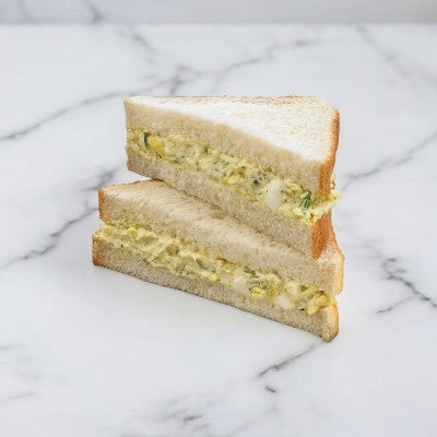 Two halves of the Dill Egg Salad On Homestyle White Bread Sandwich Wedge by E.A. Sween are stacked on a marble surface.