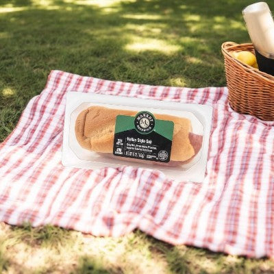 E.A. Sween's Italian Style Sub on a red and white checkered picnic blanket next to a wicker basket with an apple and a bottle inside.