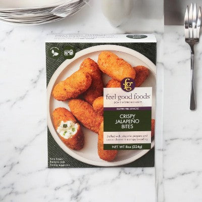 A box of Easy Lunches' "Feel Good Foods - Crispy Jalapeno Bites" (1 Box - 8 oz) featuring a spicy jalapeno filling and creamy texture, displayed on a white marble surface next to a fork and knife. Perfect for snack time!