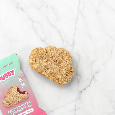 A cloud-shaped Chubby Snacks Peanut Butter & Strawberry Jam, weighing in at 2 oz, rests on a marble surface next to its partially visible green and pink packaging, highlighting its benefits of protein and fiber.