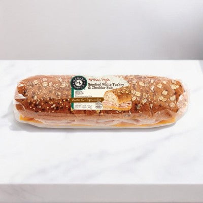 Plastic-wrapped sandwich on a white surface. Label reads “E.A. Sween Smoked Turkey & Cheddar Sub Sandwich On Rustic Oat Topped Roll.”