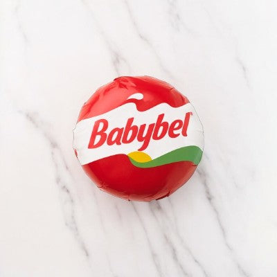 A small round package of Mini Babybel Original Semisoft Cheese- 1 Piece, wrapped in red wax and placed on a white marble surface, delivers the creamy taste that only real cheese from Babybel can offer.