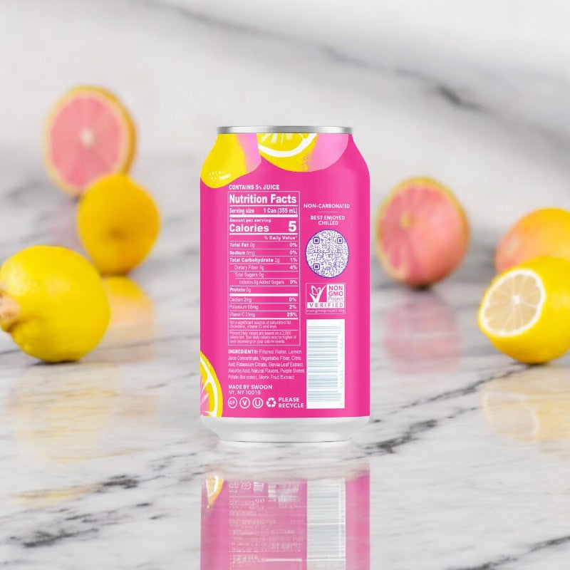 A can of Swoon Pink Lemonade by Swoon sits on a marble surface, with its nutrition facts and ingredients displayed on the back. Lemons and halved grapefruits are artfully scattered in the background, emphasizing this sugar-free beverage sweetened with monk fruit.