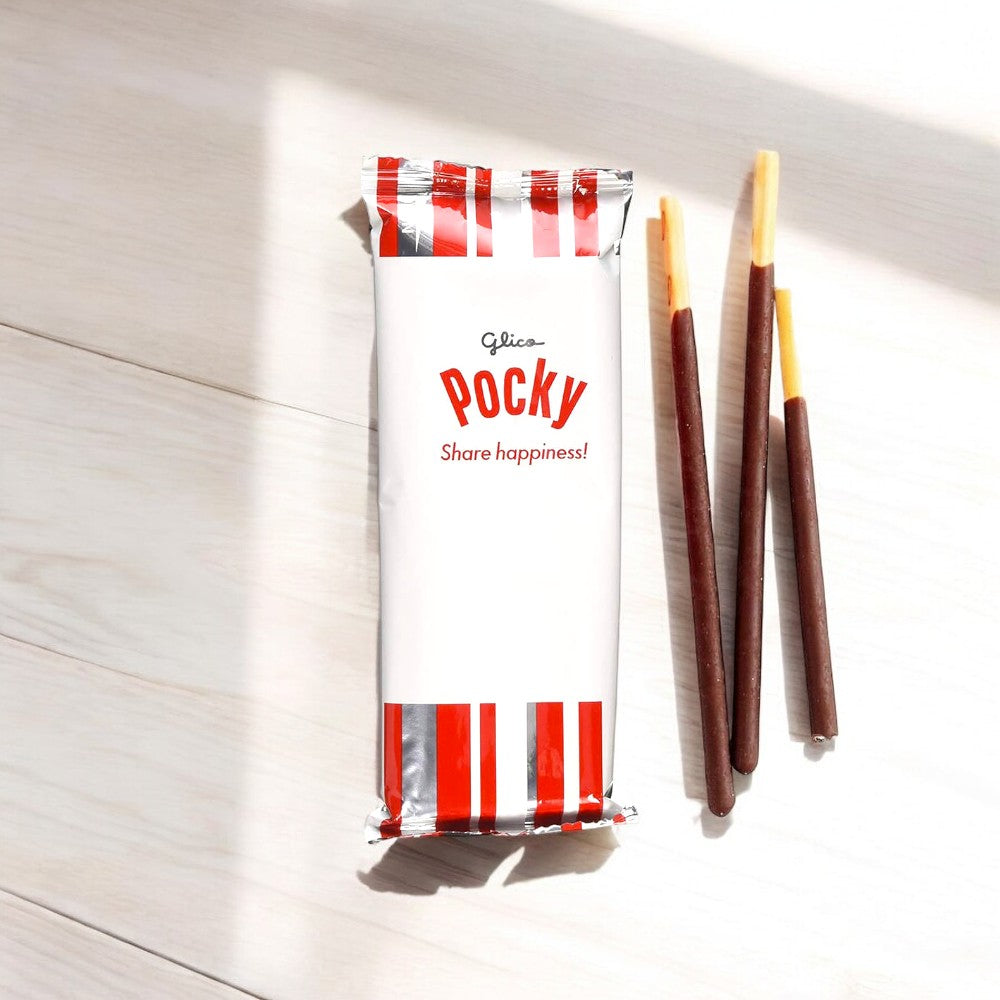 A pack of Pocky Chocolate Cream Covered Biscuit Sticks, a renowned Japanese treat, is adorned with red and white stripes and displays three biscuit sticks coated in luscious chocolate on a light wooden background.