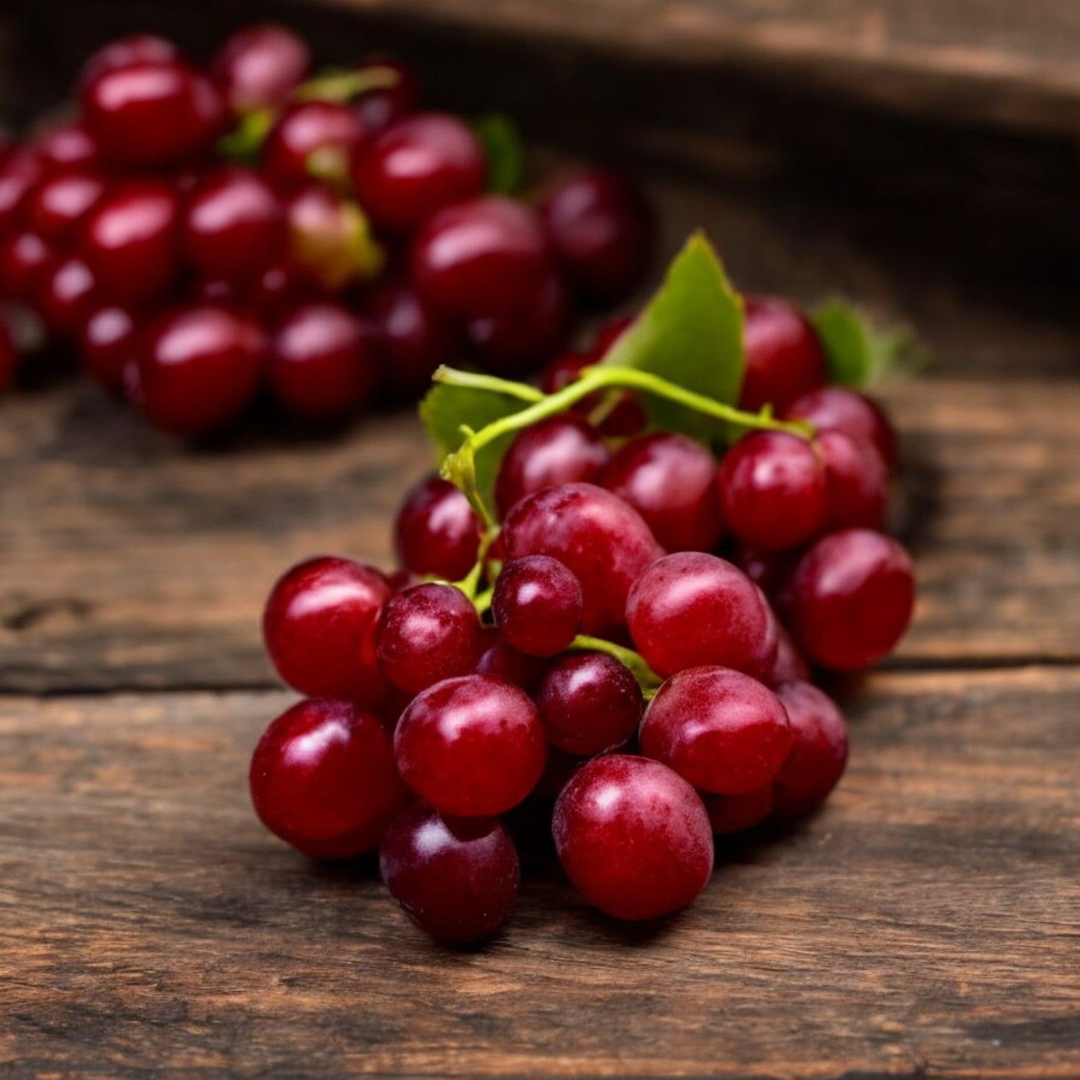 A cluster of Easy Lunches Red Seedless Grapes - 2 lbs rests on a wooden surface, with another cluster slightly out of focus in the background.