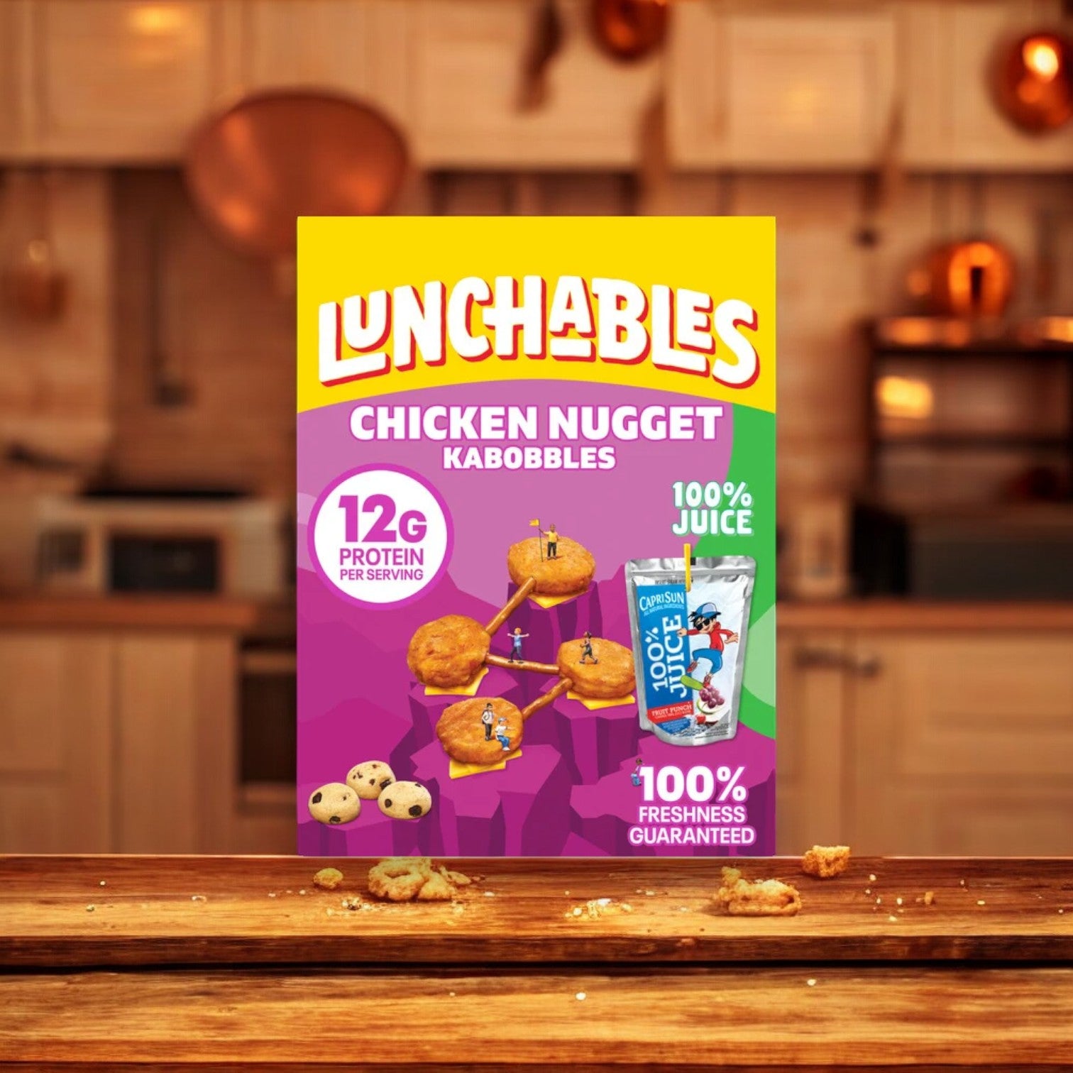 A Lunchables Chicken Nugget Kabobbles package, included in the Lunchables Variety Bundle!, is displayed in a kitchen setting. The box highlights 12g of protein per serving and comes with 100% juice. Surrounding the box are scattered food crumbs.