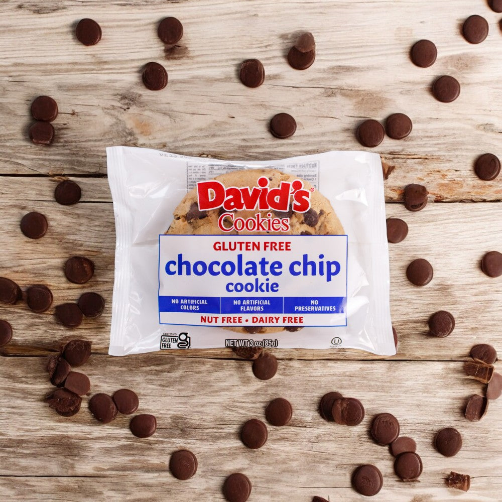 On a wooden surface, there's a package of David's Cookies Gluten-Free Individually Wrapped Chocolate Chip Cookie (3 oz - 1 count), surrounded by scattered chocolate chips. The packaging highlights that the cookie is nut-free and dairy-free, making it an excellent choice for health-conscious consumers with dietary restrictions.