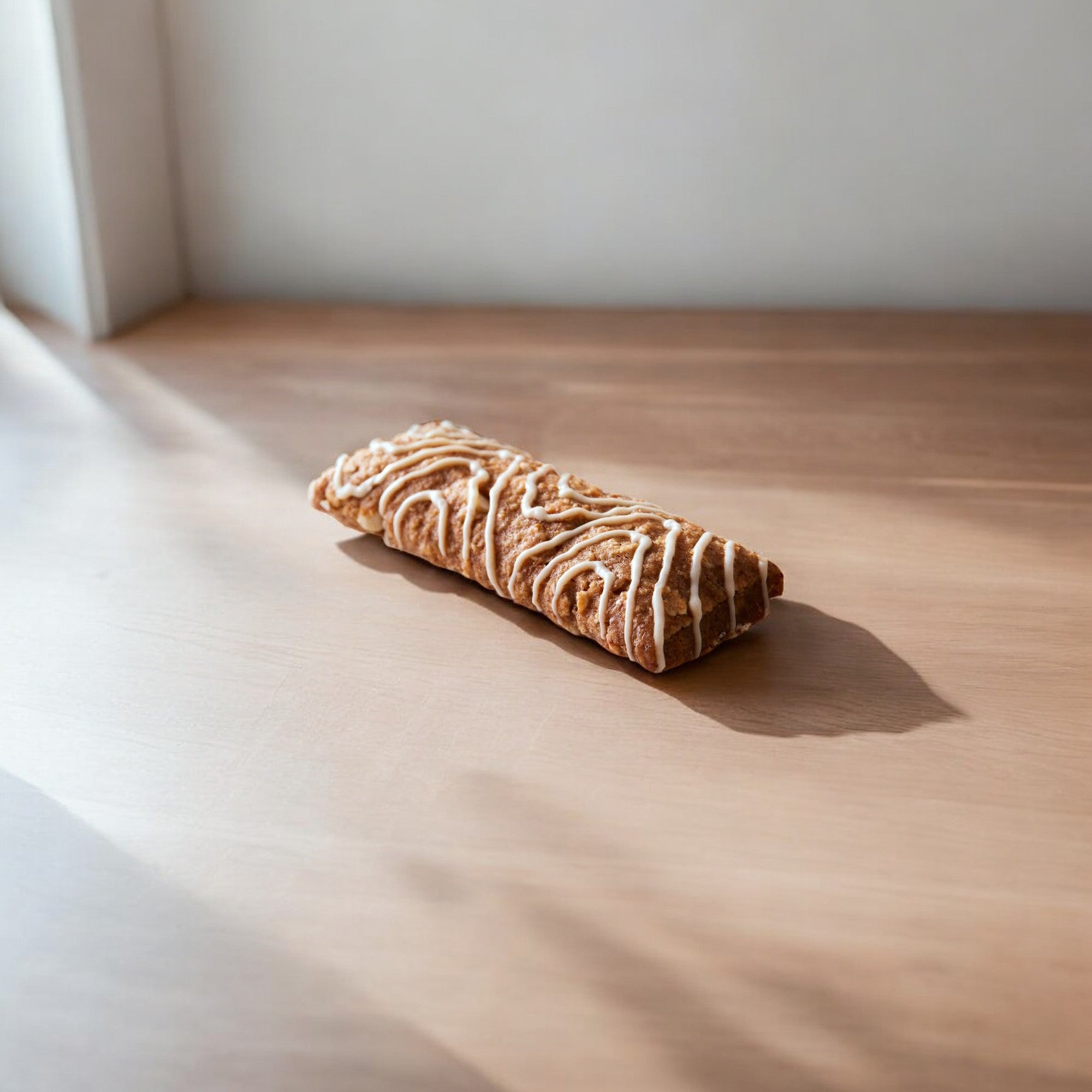 A Clif Kid Zbar Organic Iced Oatmeal Cookie Snack Bar -1.27 oz from Clif Bar rests on a wooden surface in natural light, topped with drizzled icing that makes it the perfect kids' snack bar.