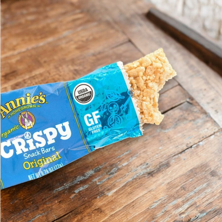 A partially eaten Annie's Organic Original Crispy Snack Bar sits on a wooden surface, with its blue wrapper highlighting that the snack is gluten-free and weighs 0.78 ounces (22 grams).