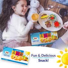 A young girl happily holds a custard cup while lying on a blanket with a plush toy. Nearby, there are snacks arranged on a plate, including the healthy "Dole No Sugar Added Mixed Fruit Variety Pack, 4 oz, 16 Pack" from Dole.