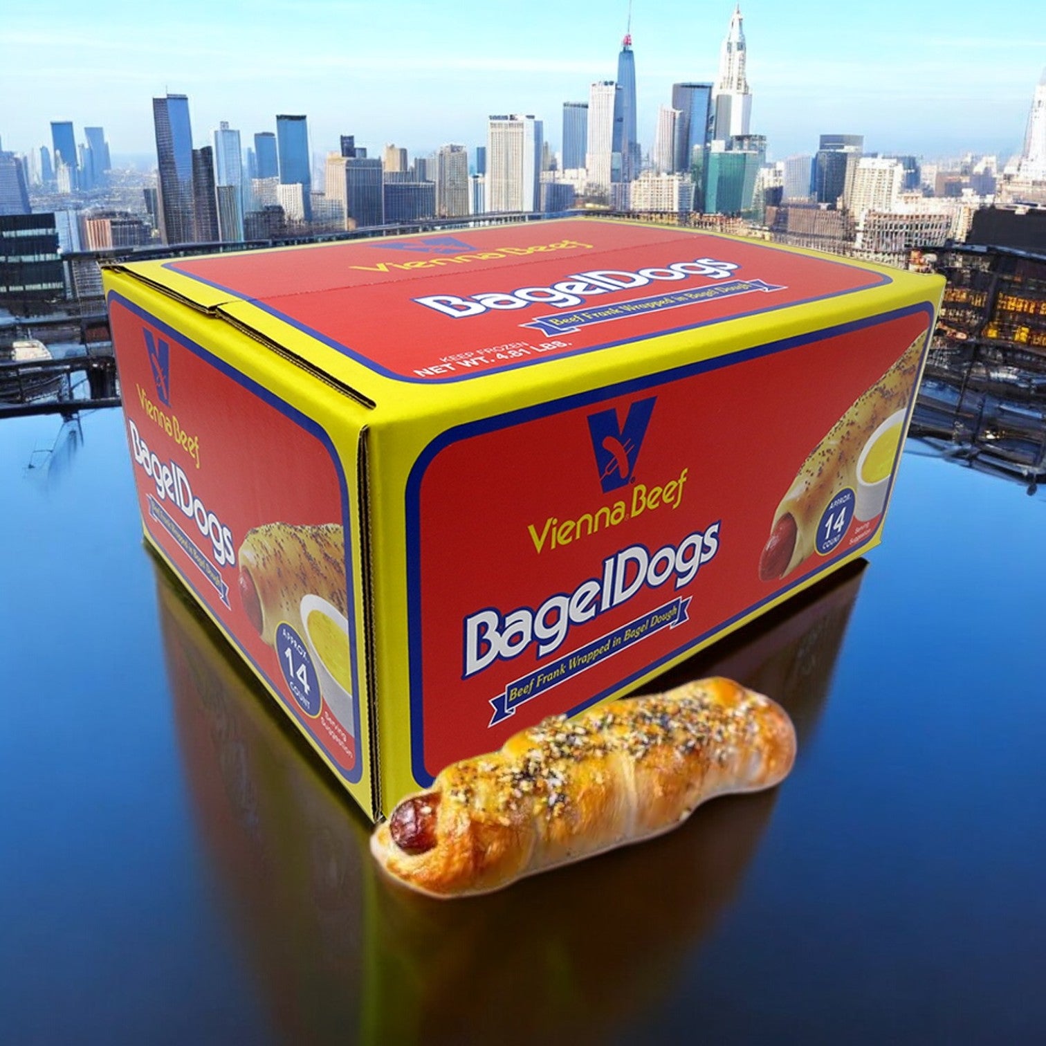 A package of Vienna Beef Bagel Dogs- 1 Count rests on a reflective surface, beautifully mirroring the essence of the city skyline in the background. One mini bagel-wrapped delight stands front and center, highlighting the tempting appeal of these hot dogs from Vienna Beef.