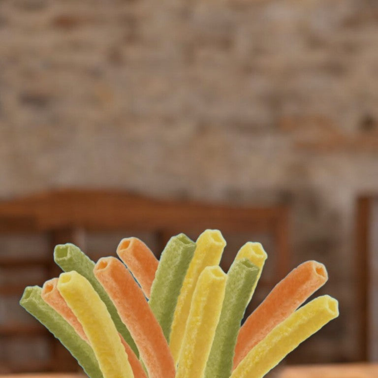 A close-up of Hain Celestial's Garden Veggie Straws Cheddar Cheese – 1 oz – 1 Count, showcasing the vibrant orange, green, and yellow pieces against a blurred, rustic background, offers a lively display of this vegetable and potato snack.