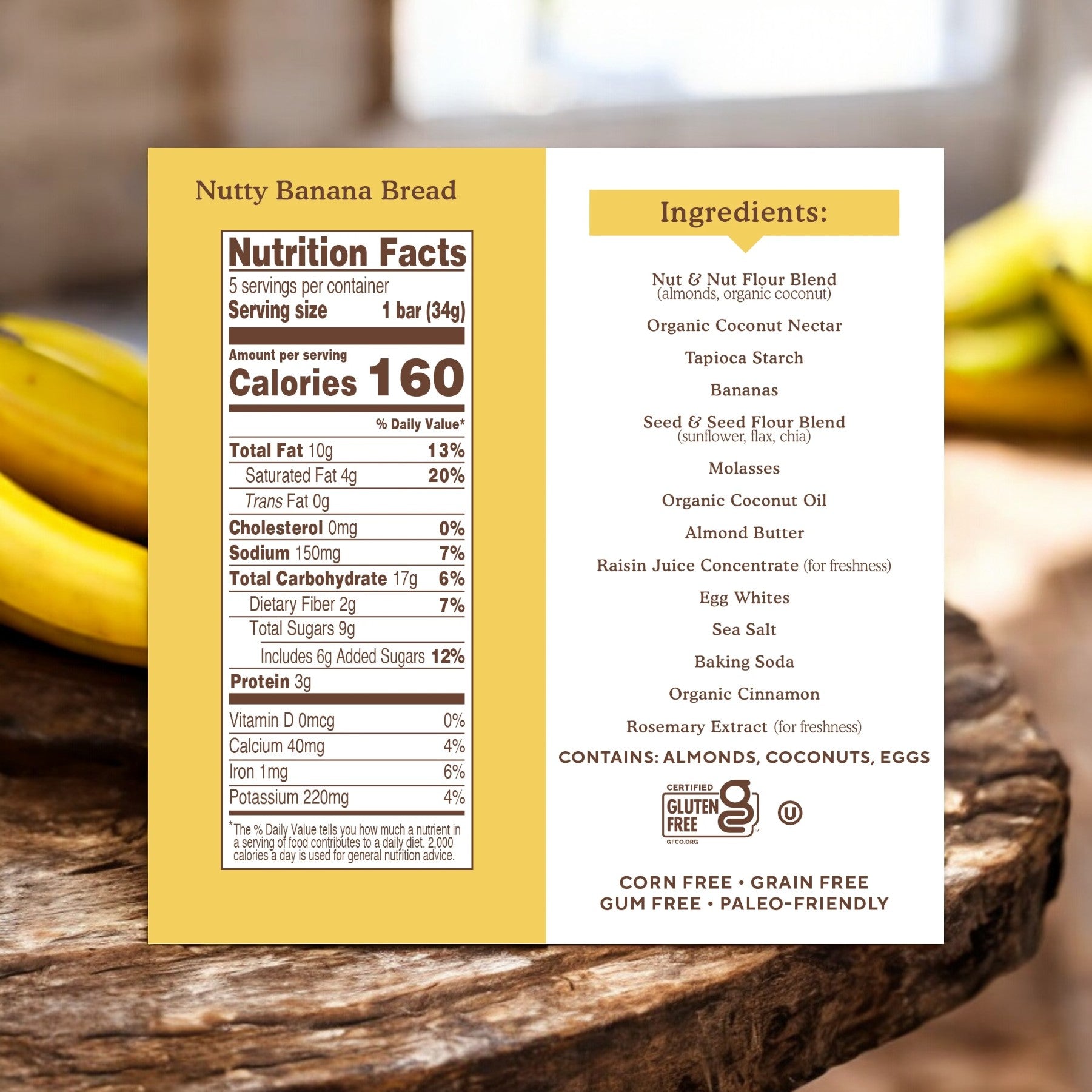 A packaged Simple Mills Soft Baked Almond Flour Bars, Nutty Banana Bread, featuring a label with detailed nutrition facts and an ingredient list. The product is gluten-free, grain-free, gum-free, and paleo-friendly. The background displays bananas on a wooden surface along with almond flour bars.