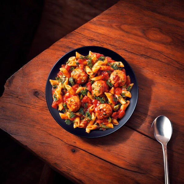 A Healthy Choice Simply Steamers Meatball Marinara sits on a wooden table next to a spoon, offering an inviting alternative to a microwaveable meal.