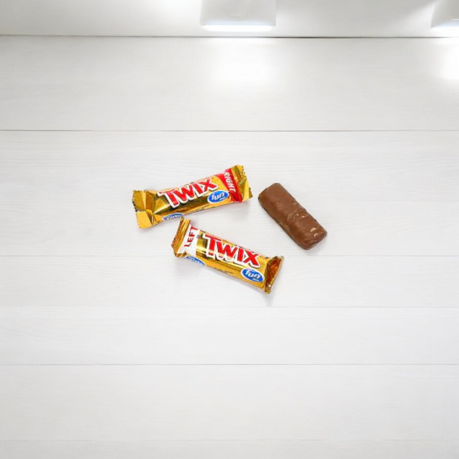 Two unopened Fun Size Twix bars from a Mars 5 Count package and a single opened chocolate bar are placed on a white surface.