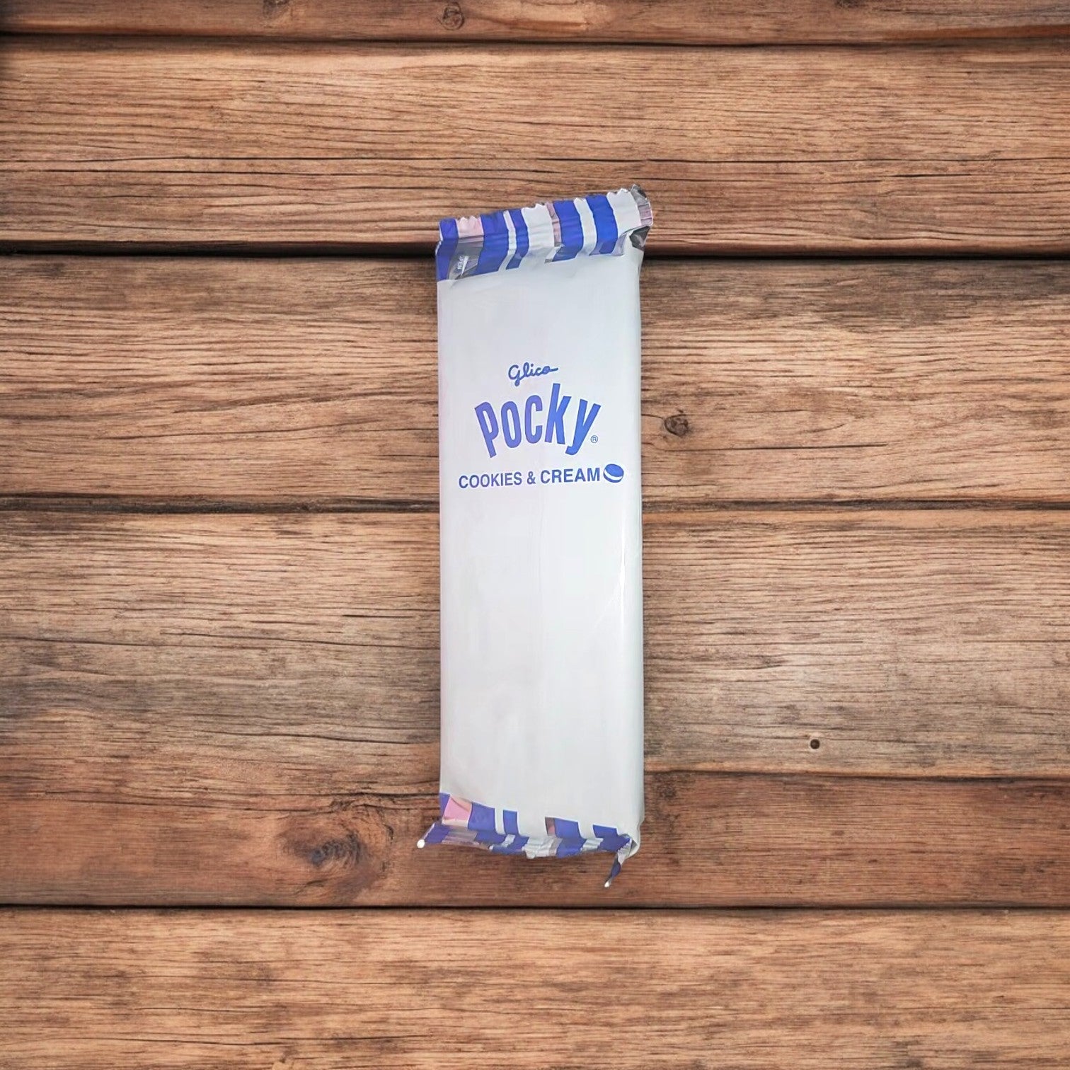 A package of Pocky Biscuit Sticks Covered in Cookies & Cream, 1.41 oz – 1 Pack rests on a wooden surface, featuring a light chocolate coating.