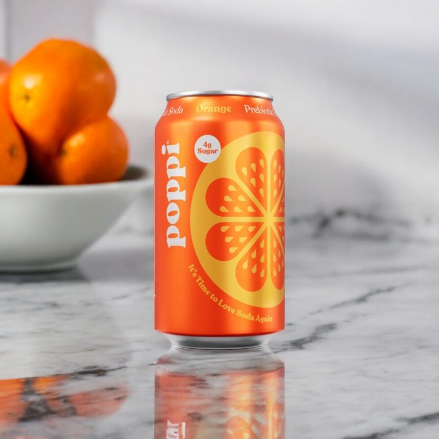 A can of Poppi Prebiotic Soda, Orange (12 fl oz), featuring low-calorie and healthy ingredients, sits on a marble surface next to a bowl of fresh oranges.