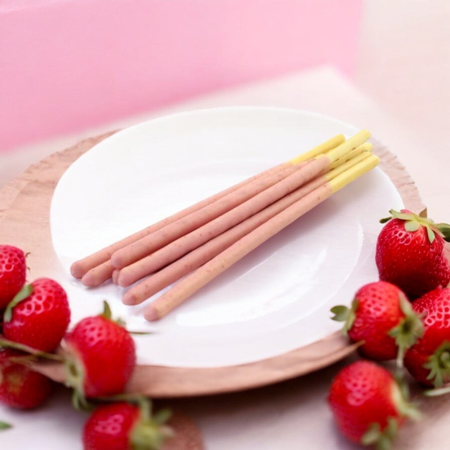 Pocky Strawberry Cream Covered Biscuit Sticks, from the well-loved Pocky brand, rest on a white plate surrounded by fresh strawberries.