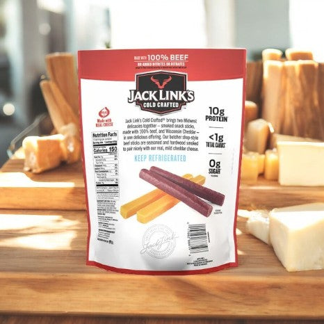 A package of Jack Link's Cold Crafted Beef Stick & Mild Cheddar Cheese Combo - 1 Count rests on a wooden table, ideal for on-the-go snacking, with mild cheddar cheese and a selection of other cheeses elegantly displayed in the background.