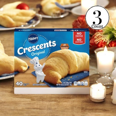 A package of Pillsbury Crescents - 3 Count rests on a table, filling the air with the delightful scent of freshly baked croissants and their rich, buttery layers. Nearby, candles dance softly in the flickering light, adding a cozy ambiance to the decorative items around. Ideal for those who appreciate pre-made dough and easy baking pleasures.