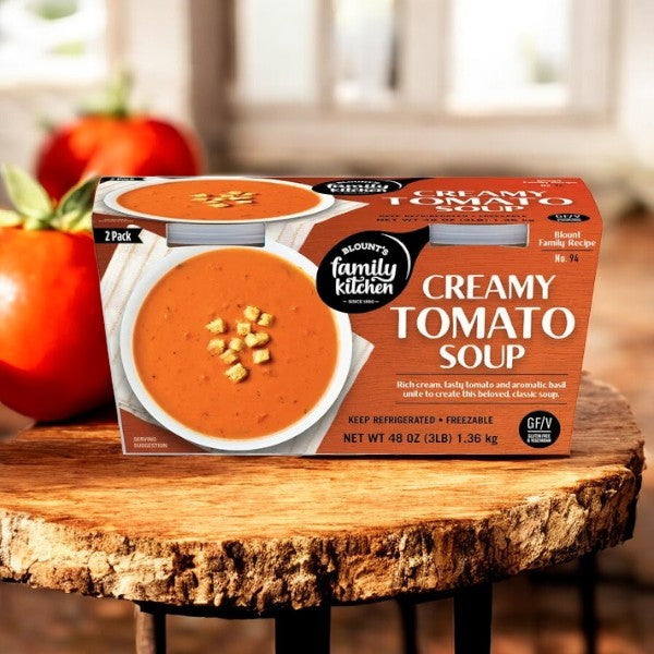 Blount's Family Kitchen Creamy Tomato Soup, from Blount Fine Foods, is shown with two bowls on a wooden surface surrounded by fresh tomatoes. Enjoy the homemade taste made with high-quality ingredients. Comes in 24 oz packages, 3 per set.