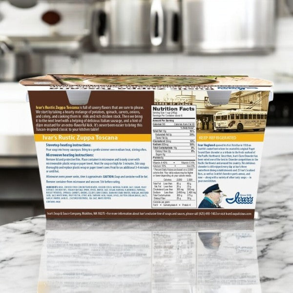 A box of Ivar's Rustic Zuppa Toscana Soup, a 24 oz Tuscan-themed soup with creamy chicken stock and Italian sausage, is on a marble countertop. The packaging displays nutritional info and vibrant images like a transportation scene and a person in a hat.