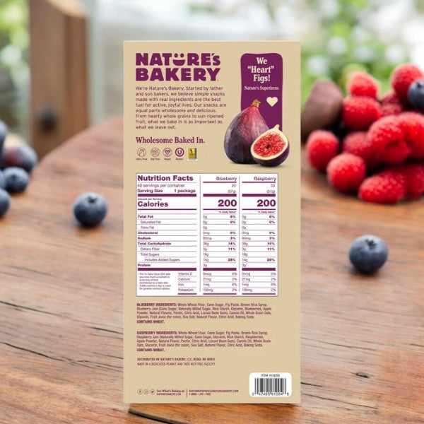 Box of Easy Lunches Nature's Bakery Fig Bar, Variety Pack - 3 Cases showing the nutrition facts side, placed upright on a wooden table with blueberries and raspberries in the background.