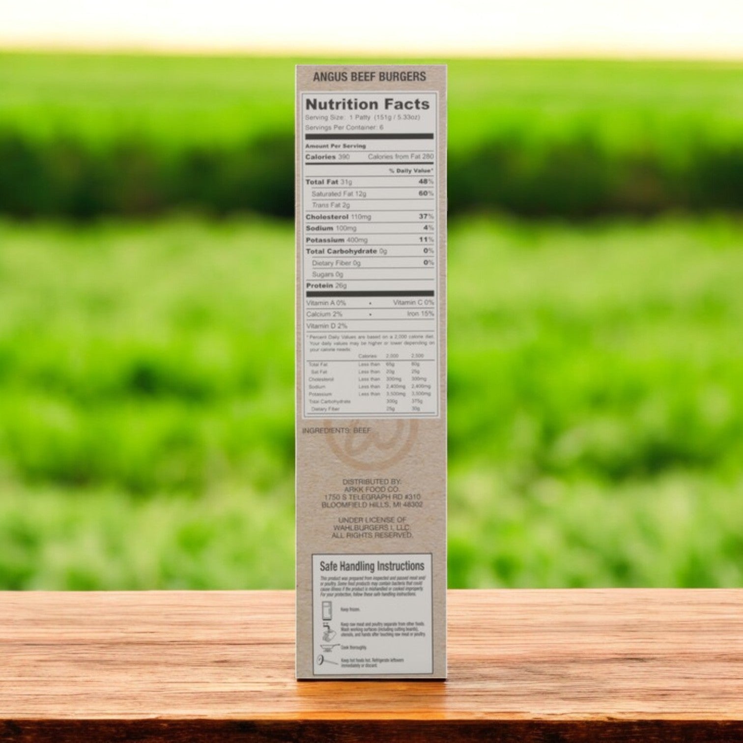 Three boxes of Wahlburgers Angus Beef Burgers, Original, 6 ct, 32 oz each, are displayed on a wooden table. The restaurant-quality flavor is highlighted alongside visible nutrition facts and handling instructions, set against a blurred green field backdrop.