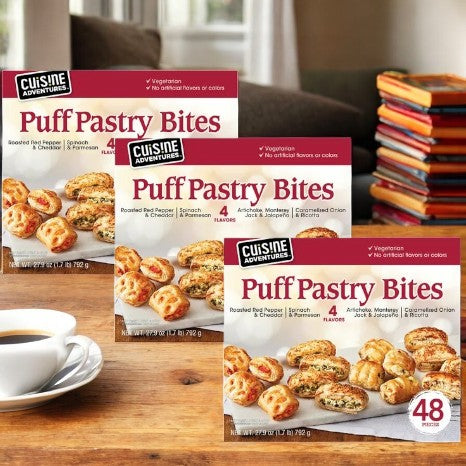 A box of Cuisine Adventure's Puff Pastry Bites Variety Pack, containing three delightful flavors, is elegantly displayed next to a cup on the table.