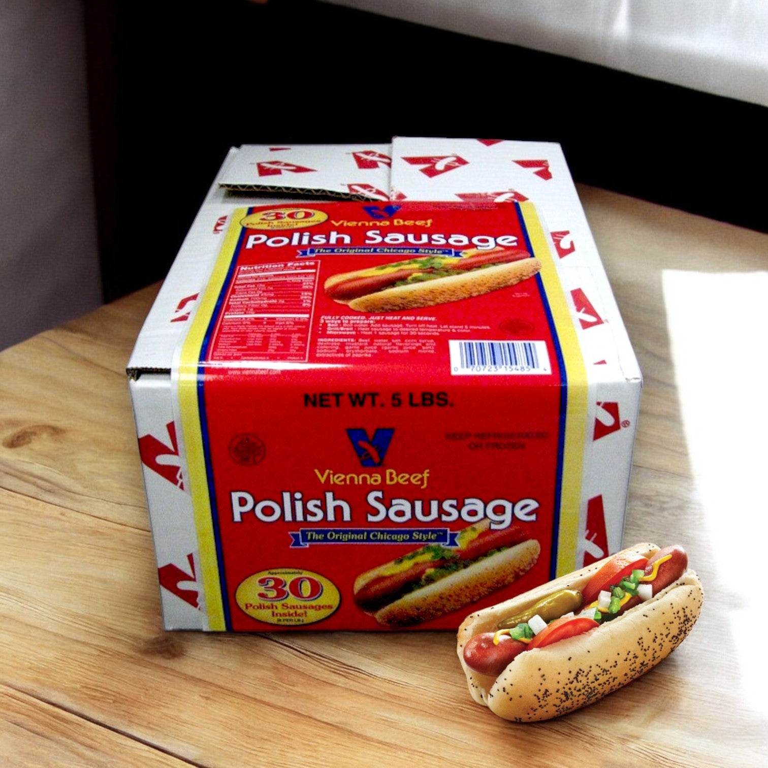 A box of Vienna Beef 6" Skinless Polish Beef Sausage (30 count) sits on the table beside a Chicago-style hot dog packed with premium beef, mustard, relish, onions, and a pickle slice in a poppy seed bun.