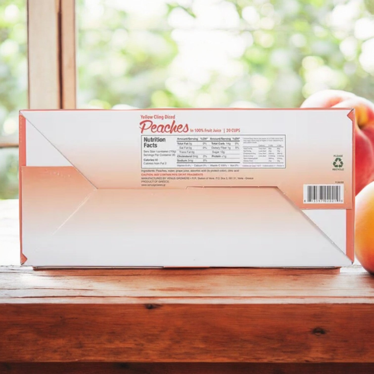 A box of Easy Lunches Venus Growers Diced Peach Cups, 4 oz, 20 Count is placed on a wooden surface in front of a window. Nutritional facts and product information are printed on the side of the box.