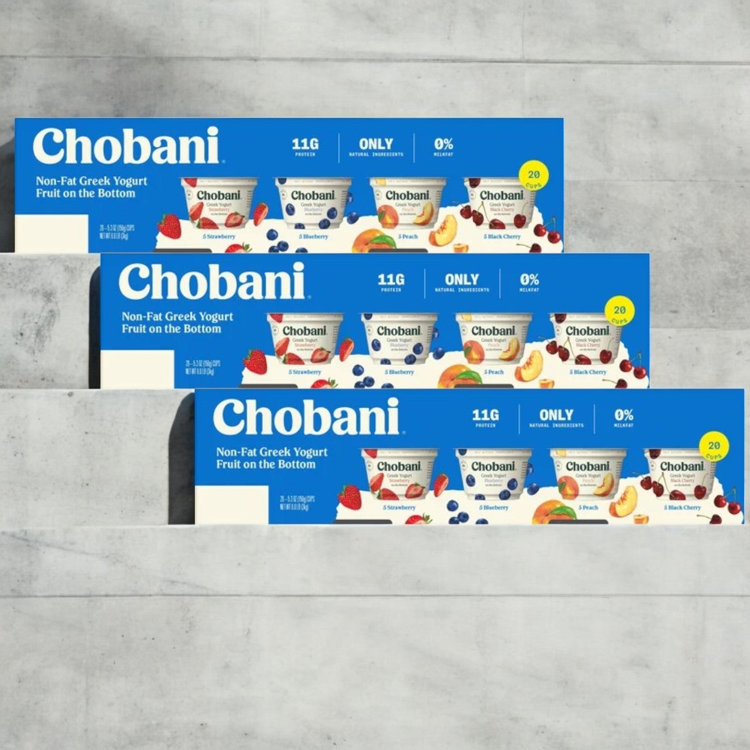 Three boxes of Chobani Greek Yogurt Variety Pack (5.3 oz, 60-count) featuring protein-rich raspberry, strawberry, and peach flavors are stacked against a light stone background.