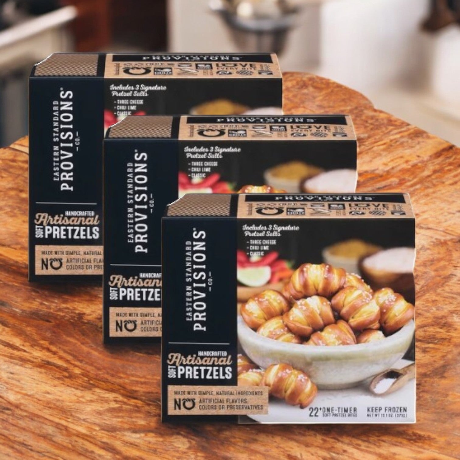 Three boxes of Eastern Standard Provisions Pretzel Bites are elegantly displayed on a wooden surface, each offering a chewy snack made from premium ingredients.