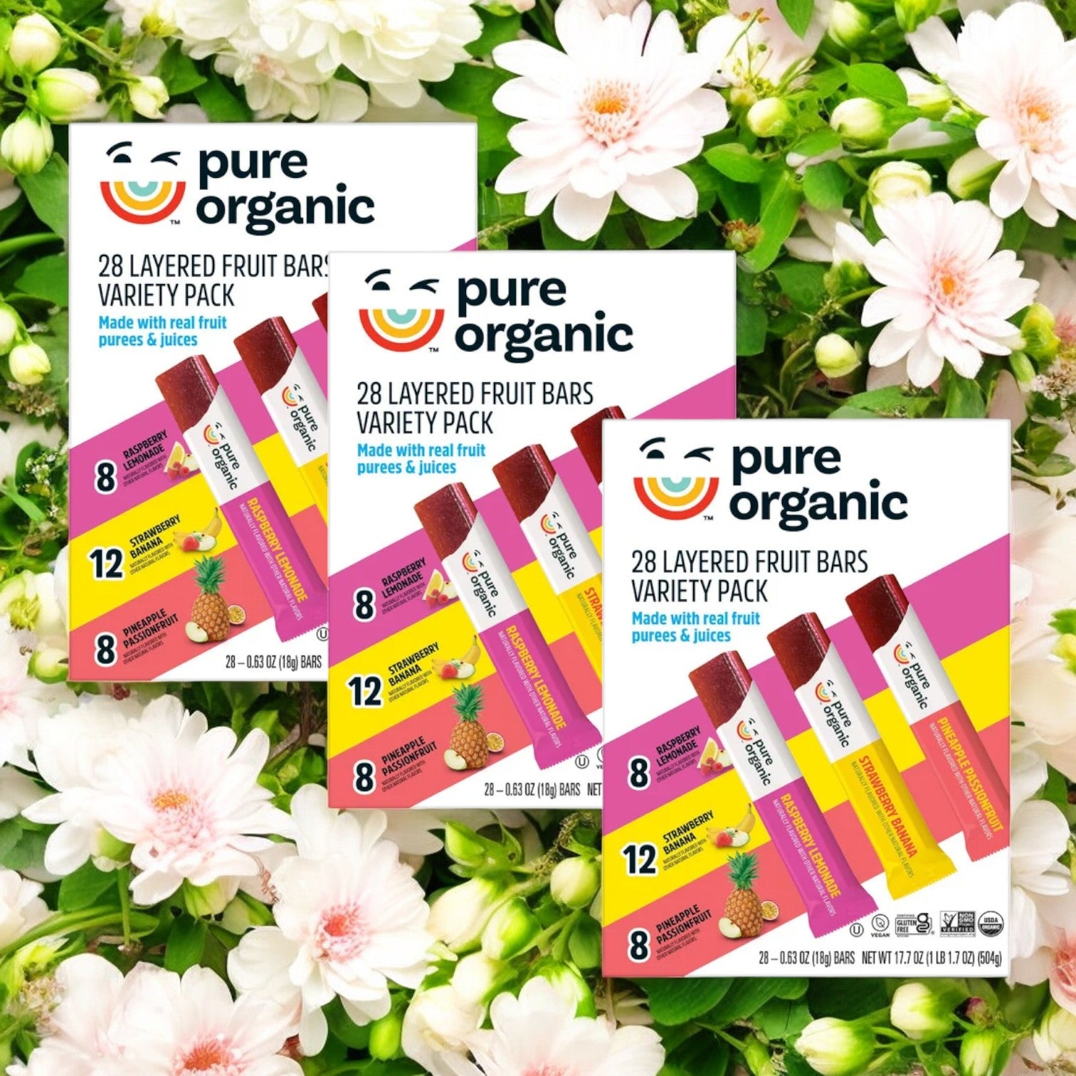 The Pure Organic 28 Layered Fruit Bars Variety Pack, consisting of three boxes and totaling 84 bars, is tastefully displayed against a backdrop of white flowers, creating a picturesque scene for this wholesome snack.