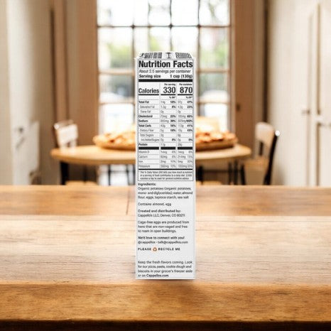 A box of Cappello's Gnocchi Pasta - 3 Count, with its nutrition facts clearly visible, is resting on a wooden table against a blurred backdrop featuring a dining area and windows.