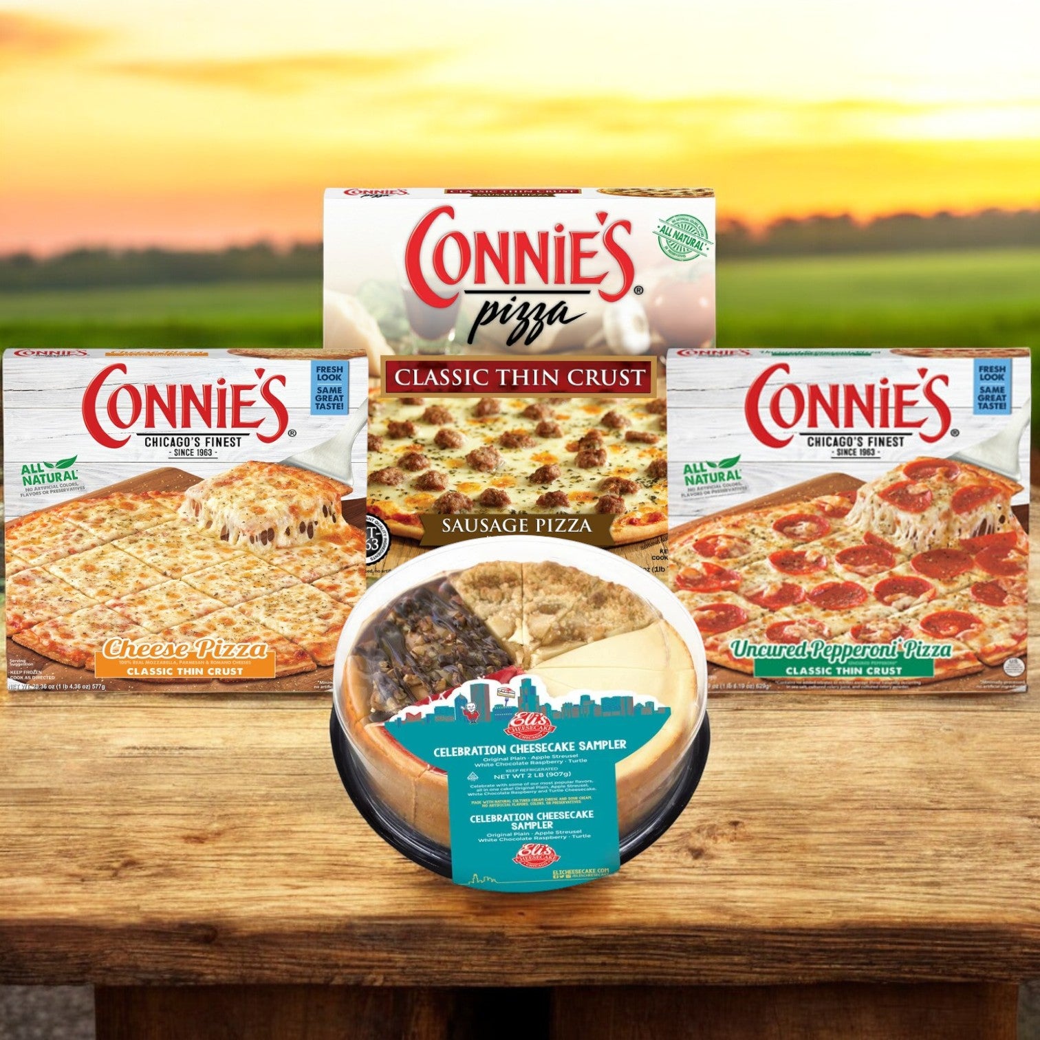 On a wooden surface with a field and sunset in the background, you can see the Connie's Bundle from Easy Lunches. This bundle includes four pizza boxes featuring thin crust pizzas and a plain cheesecake sampler, making it the ultimate package for any gathering. Plus, enjoy free shipping on this delightful offer.