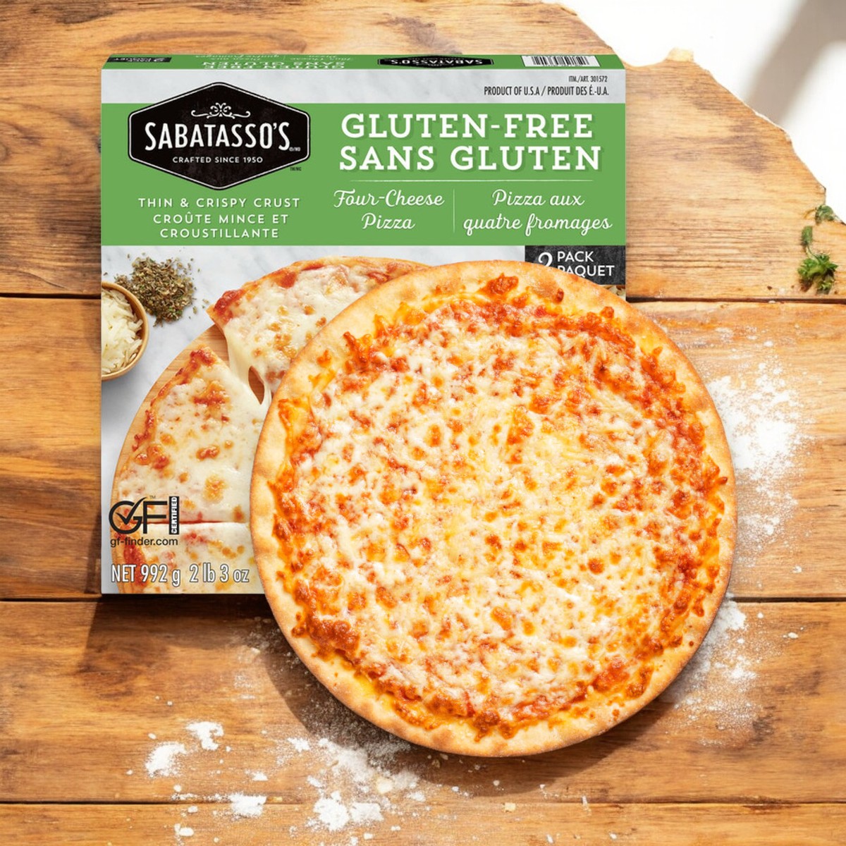 A freshly baked Sabatasso's Four Cheese Pizza from the 3-Pack collection sits on a wooden table next to its packaging, which proudly displays the Sabatasso's brand and emphasizes its gluten-free, thin and crispy crust.